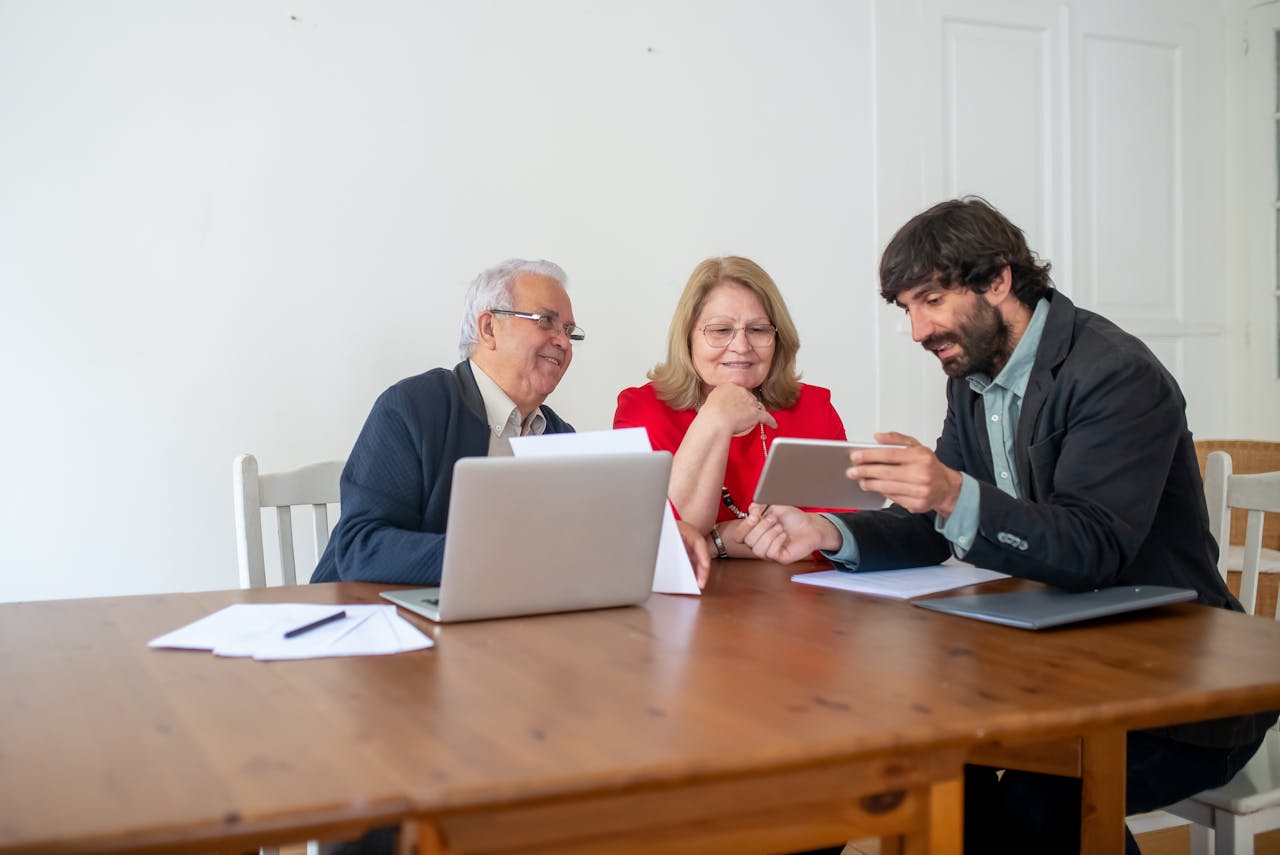 About Two senior clients and a consultant discussing documents and using a tablet in a modern office.